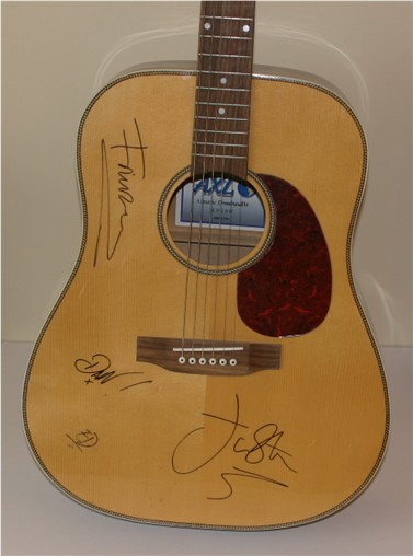 This is an acoustic guitar which has been hand signed in black pen by all four members of the rock
