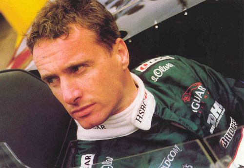 Eddie Irvine in his Jaguar Formula one overalls sat in a classic Jaguar